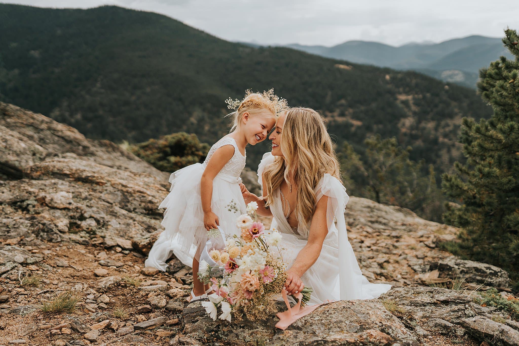 bride and flowergirl laughing on a mountain top with flower crowns and whimsical dresses at Northstar Gatherings in Idaho Springs
